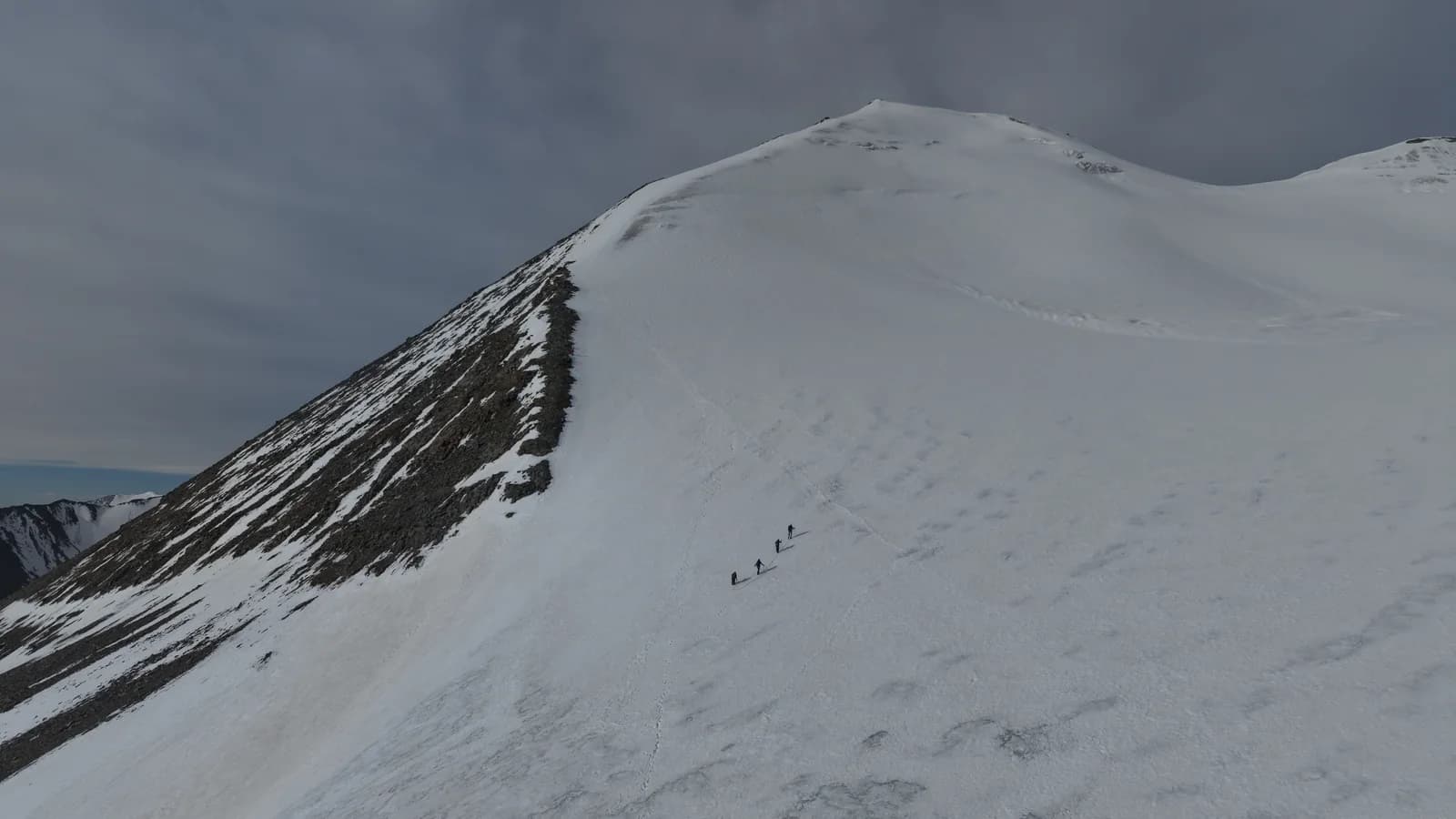 Climbers following a track across a broad snow-covered mountain slope