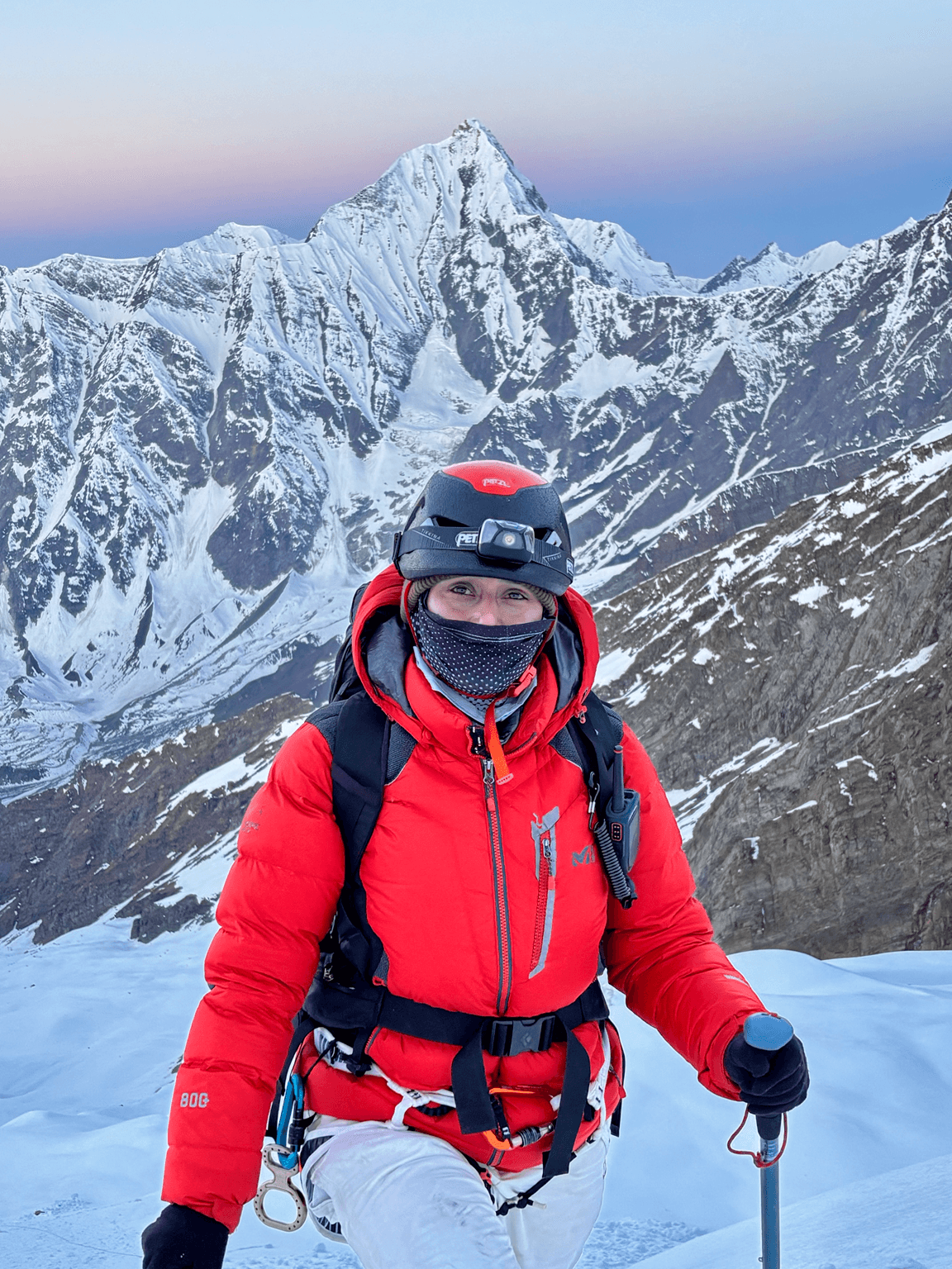 Nikita Thakur in red expedition gear below a snowy Himalayan peak